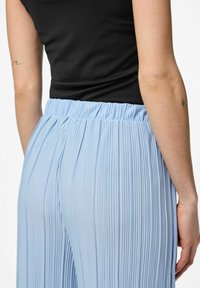 Ljusblå veckade byxor med resårmidja; tillsammans med en figurnära svart topp. Tyget ser slätt ut med fina vertikala linjer.