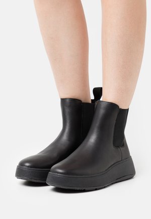 Schwarze Leder-Stiefeletten mit elastischen Seiteneinsätzen, runder Zehenpartie und einer dicken Gummisohle. Glatte Textur ohne sichtbare Muster oder Hardware-Details.