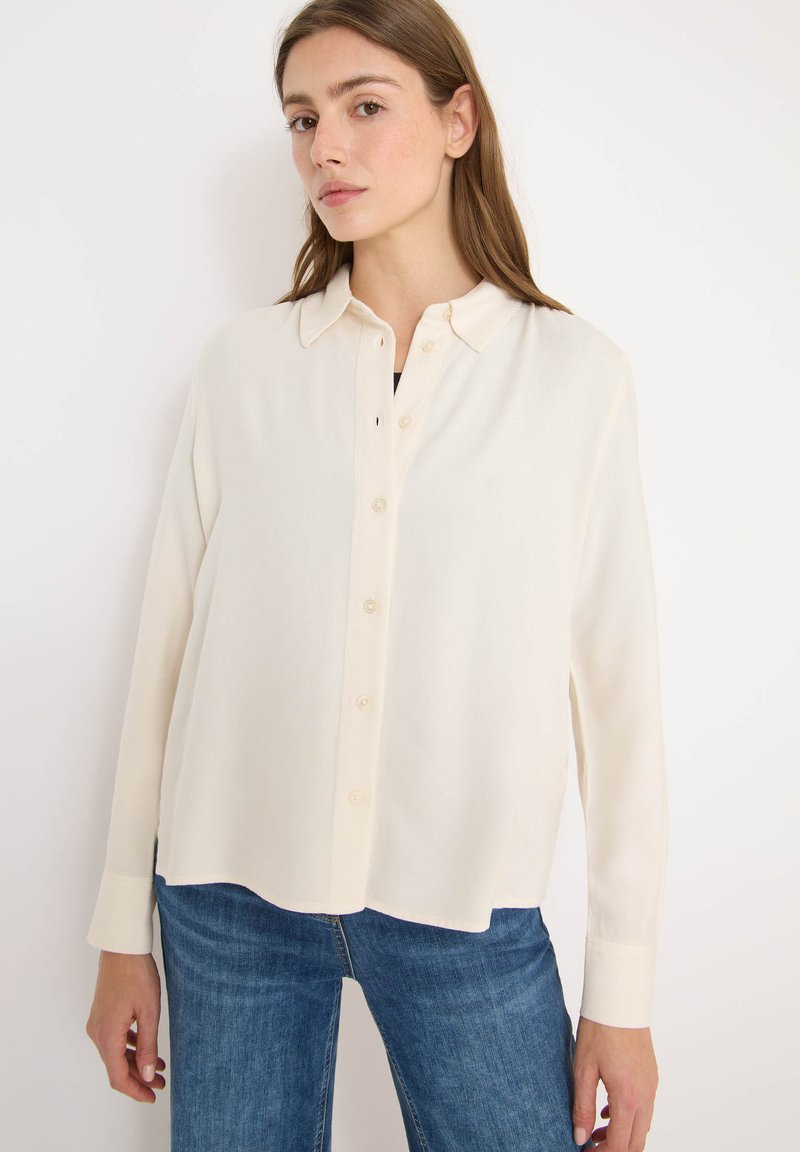 Cremefarvet skjorte med knaplukning lavet af blødt stof, med krave, lange ærmer og lige pasform, kombineret med blå denim jeans.