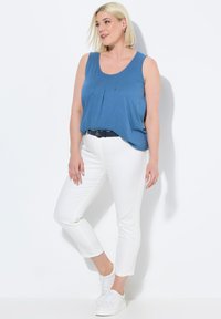Top sin mangas azul con plisados, combinado con jeans blancos hasta los tobillos y zapatillas blancas, con un diseño simple y colores sólidos.