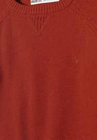 Maglione rosso a maglia con scollatura rotonda, polsini a coste e un discreto dettaglio del logo sul petto. Texture liscia e design aderente.