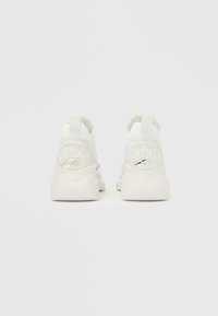 Weiße Sneaker mit einem glatten Stoffobermaterial und einem strukturierten Fersenbereich. Verfügen über eine Zuglasche und silberfarbene Beschläge.