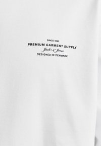 T-shirt bianca in cotone con stampa nera: "PREMIUM GARMENT SUPPLY," "Jack & Jones," e "DESIGNED IN DENMARK." Texture liscia.