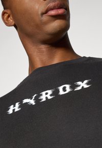 Black cotton short-sleeve shirt featuring a white distressed "HYROX" logo across the chest. Smooth texture with a classic crew neckline.