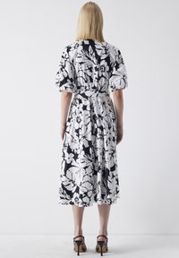 Blommönstrad klänning i svart och vitt, med korta puffärmar, en tajt midja och flödande kjol. Bärs med strappy högklackade sandaler.