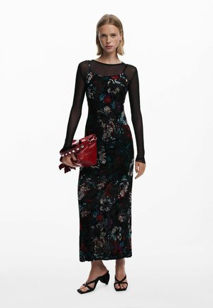 Abito nero floreale con corpetto aderente, maniche lunghe trasparenti e silhouette dritta. Abbinato a una borsa a tracolla rossa in pelle con borchie argentate.
