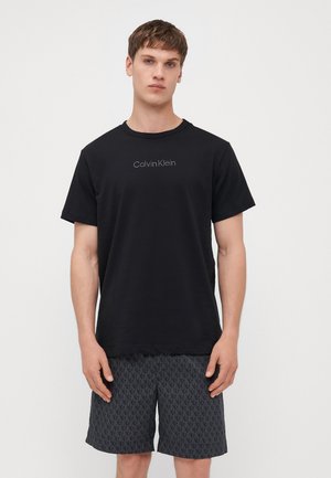 Juodas medvilninis marškinėliai su apvalia iškirpte ir trumpomis rankovėmis, priekyje yra subtilus pilkas "Calvin Klein" logotipas.