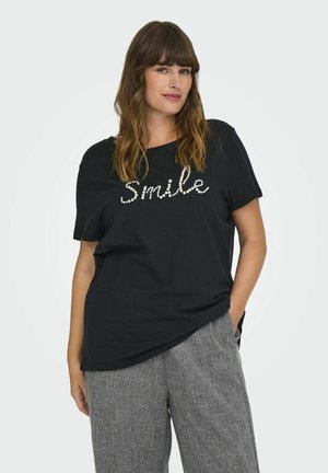 Camiseta negra de manga corta con un diseño de "Sonrisa" hecho de cuentas decorativas. Combinada con pantalones texturizados de color gris claro.