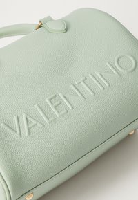 Světle zelená texturovaná kožená kabelka s vyraženým logem "Valentino", zaoblený tvar a zlaté akcenty hardware.