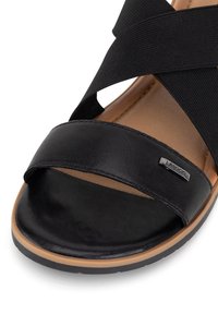 Black sandal with elastic crisscross straps, a wide leather band across the toe, cushioned insole, and a rubber outsole. Silver logo detail present.