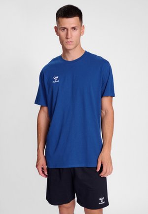 Blauwe katoenen T-shirt met een ronde hals en korte mouwen, met een klein wit logo op de linkerkant van de borst. Gecombineerd met zwarte shorts.