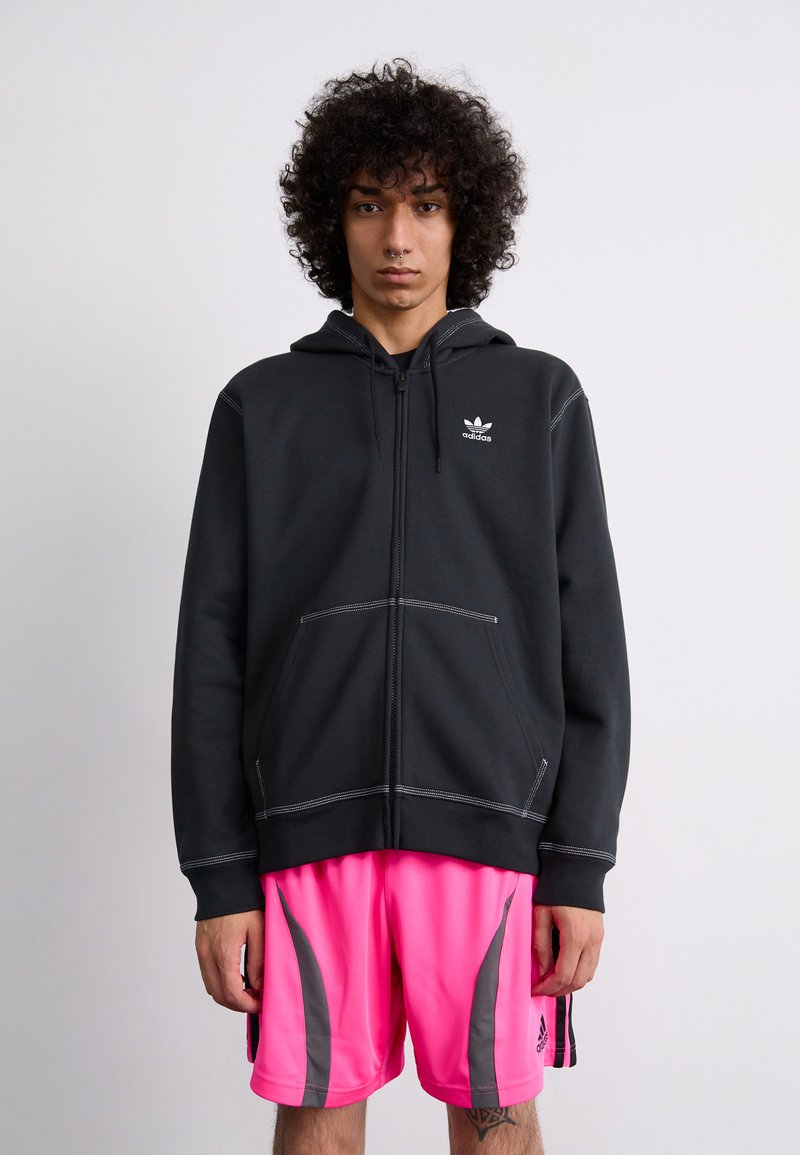 Sweatshirt preto com fecho, costura branca e bolsos frontais, combinado com calções rosa neon com detalhes cinzas e riscas laterais.