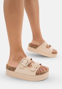 Beige plattformsandaler med en texturerad korksula. Har två spännen prydda med klara stenar och en mjuk mockaöverkänsla.