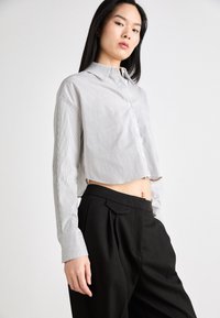 Camicia abbottonata cropped con sottili righe verticali bianche e nere, maniche lunghe e colletto classico, abbinata a pantaloni neri a vita alta.