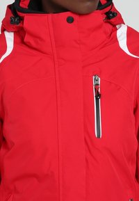Rote isolierte Jacke mit hohem Kragen, weißen Akzenten, einer Brusttasche mit Reißverschluss und verstellbaren Zugkordeln an der Kapuze und dem Saum.