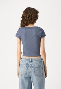 Modrý rebrovaný crop top s krátkymi rukávmi, skombinovaný s vysokými džínsami s ľahkým praním, ktoré majú zadné vrecká a voľný strih.
