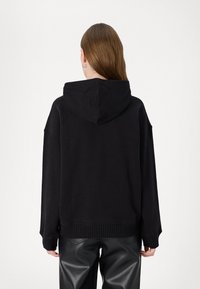 Felpa nera con orlo e polsini a costine, dotata di cappuccio con coulisse e design oversize. Tessuto morbido con una texture liscia.