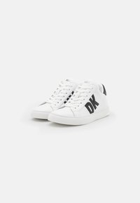 Hvite lær sneakers med svart DK-logo, rund tå, snøring, og teksturerte detaljer på hælen. Flat gummisåle.