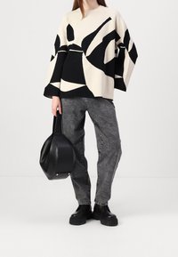 Pull surdimensionné noir et blanc avec des formes abstraites, associé à un jean gris et un sac à main rond noir. Stylisé avec des bottes noires épaisses.