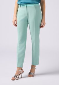 Miętowe spodnie o prostym kroju, z zamkiem błyskawicznym z przodu i zapięciem na guzik. Połączone z srebrnymi sandałami na obcasie.