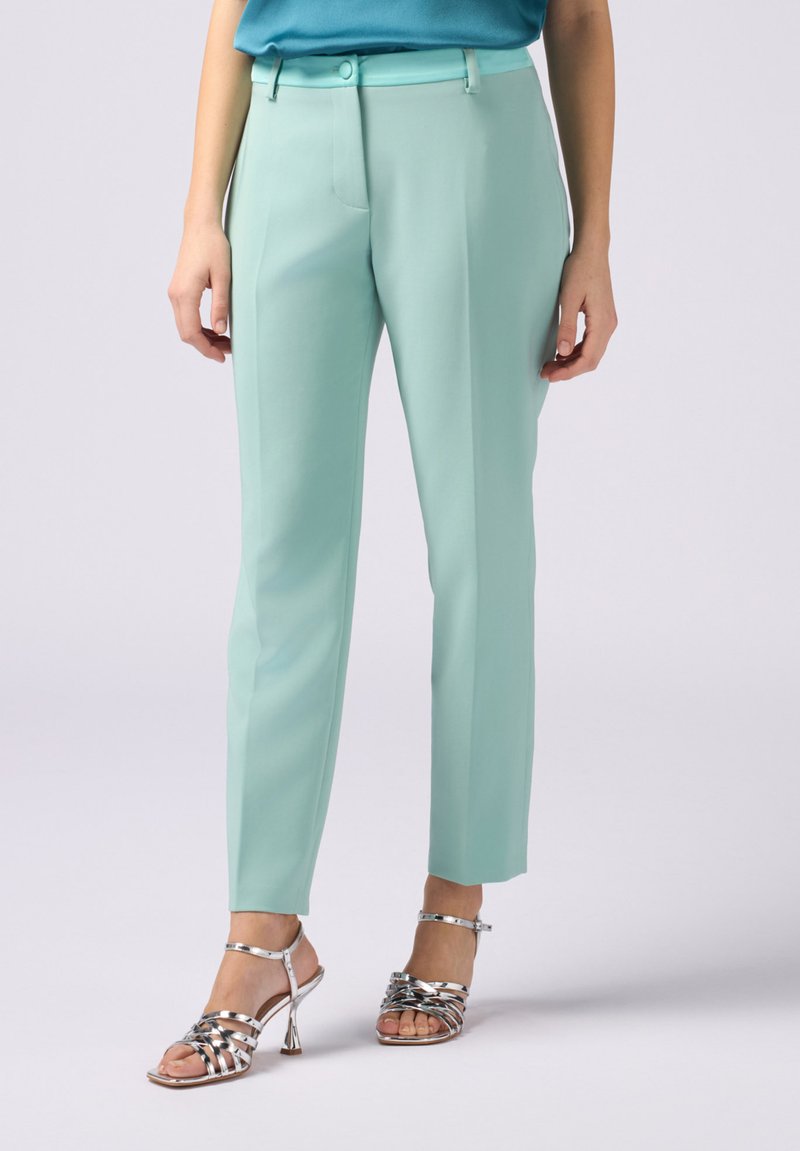 Miętowe spodnie o prostym kroju, z zamkiem błyskawicznym z przodu i zapięciem na guzik. Połączone z srebrnymi sandałami na obcasie.