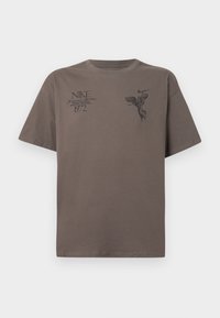 Καφέ βαμβακερό μπλουζάκι κοντομάνικο, με μαύρες γραφικές εκτυπώσεις κειμένου και σχέδιο αγγέλου στο μπροστινό μέρος. Στρογγυλή λαιμόκοψη.