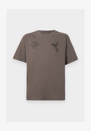 T-shirt de algodão castanho com mangas curtas, apresentando impressões gráficas pretas de texto e um desenho de anjo na parte da frente. Decote redondo.