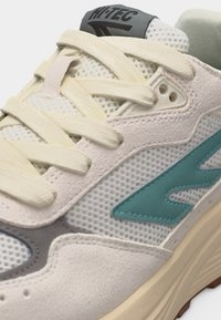 Krupan plan bež i krem tenisice s mrežastim panelima, krem vezicama, tirkiznim logotipom i natpisom "HI-TEC" na sivoj etiketi na jeziku.