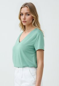 T-shirt a maniche corte, con scollatura a V, realizzato in morbido tessuto verde chiaro. Texture liscia con vestibilità rilassata, abbinato a pantaloni bianchi a vita alta.