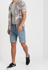 Krátký rukáv, vzorovaná košile v světle šedé barvě s motivem ptáků; pruhované šedé tričko pod tím; denimové kraťasy; černé tenisky s bílými akcenty.