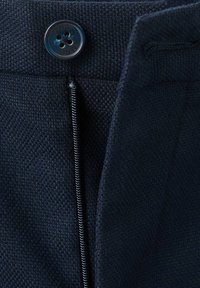 Navy modré skladané tkaniny s textúrovaným tkaním. Vybavená predným zipsom a čiernym gombíkom, zdôrazňujúcim čisté línie a minimalistický dizajn.