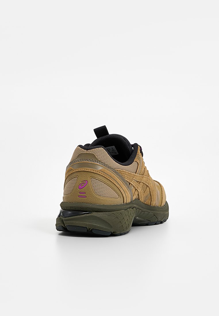 Baskets de sport beige et olive avec doublure intérieure noire, logo rose à l'arrière, et semelle texturée, présentées de l'angle arrière sur fond blanc.