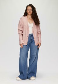Różowy kardigan z prążkowanej dzianiny o luźnym kroju, zapinany na guziki, noszony na białej bluzce z koronkowym wykończeniem i w połączeniu z niebieskimi jeansami o szerokich nogawkach.