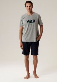 Szara bawełniana koszulka z grafiką "WILD MAN" w niebieskim i zielonym kolorze, połączona z ciemnogranatowymi szortami z elastycznym pasem.
