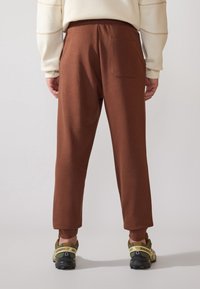 Bruna joggerbyxor med bakficka, tillverkade av mjukt tyg. Avsmalnande ben design, matchade med svarta och gula gympaskor.