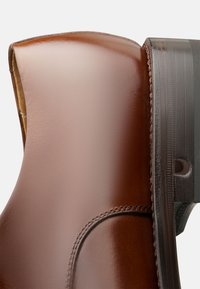 Stivale ankle in pelle marrone con una superficie liscia, punta arrotondata e una suola scura e texturizzata con cuciture in evidenza.