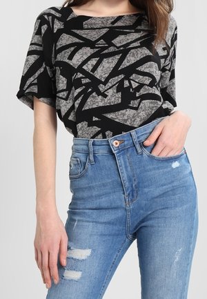 Czarna i szara koszulka z krótkim rękawem we wzory z szerokim dekoltem, w zestawie z jasnoniebieskimi, wysokim stanem, postrzępionymi dżinsami.