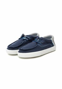 Zapatos de lona azul marino con suelas de goma blanca, punta redondeada y cordones azules. Presentan costuras texturizadas a lo largo de los bordes y acentos grises.