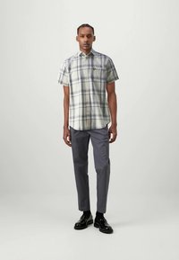 Camisa de cuadros de manga corta en colores claros con diseño de botones, combinada con pantalones grises y zapatos negros brillantes.