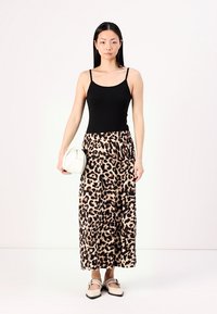 Débardeur noir associé à une jupe maxi à imprimé léopard, des chaussures plates et un petit sac à main blanc. Tissu lisse avec une taille élastique.