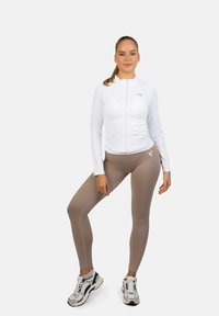 Valkoinen vetoketjulla varustettu pitkähihainen paita, jossa on hoikka malli ja harmaa logo. Vaaleanbeige korkea vyötäröiset leggingsit, joilla on sileä pinta. Mustat ja valkoiset lenkkarit.