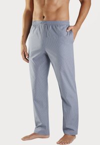 Osoba bez trička, oblečená v voľných, svetlomodrých károvan�ých pyžamových nohaviciach s elastickým pásom a šnúrkou, stojaca naboso na bielom pozadí.