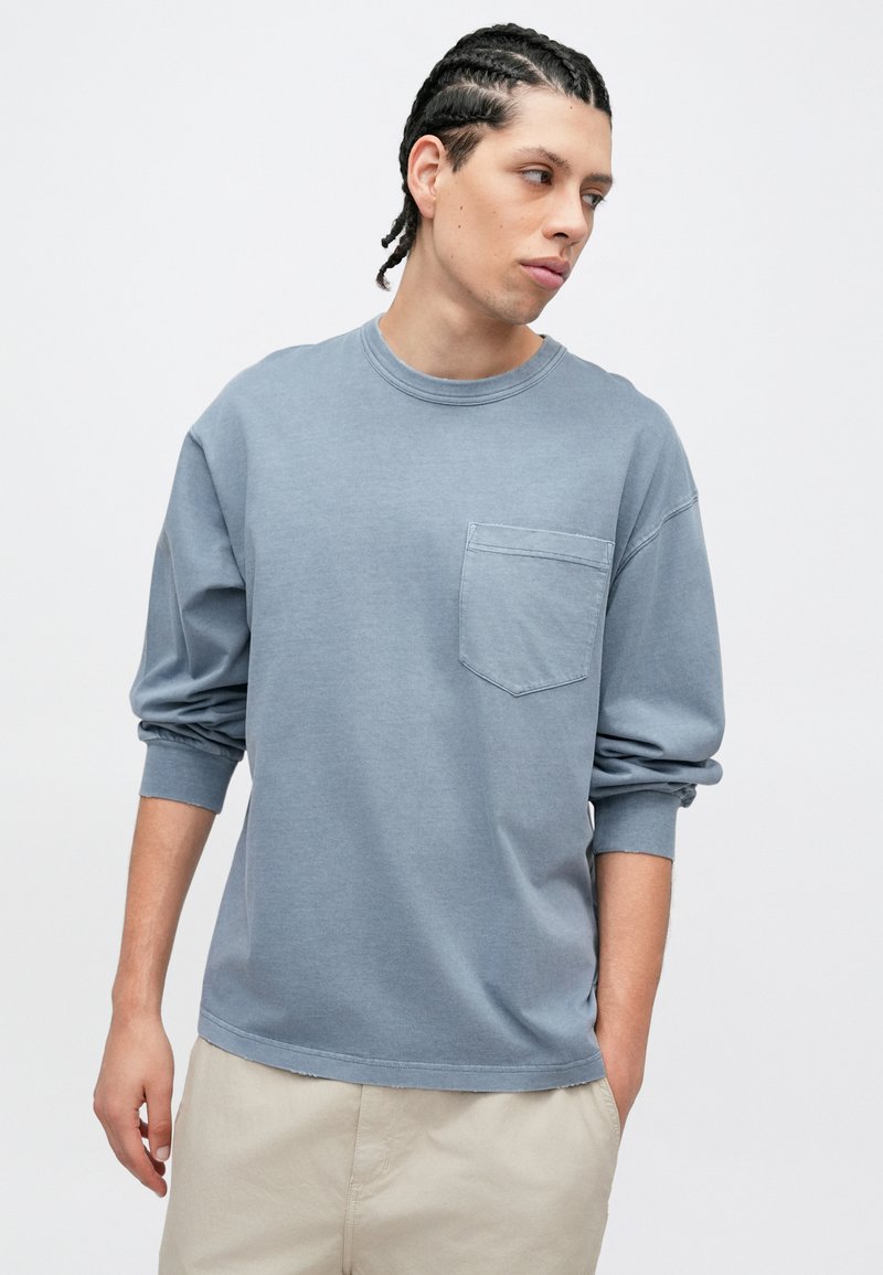 Ljusblå långärmad T-shirt i mjukt tyg, med rund halsringning och en vänster bröstficka. Avslappnad passform och ribbade muddar.