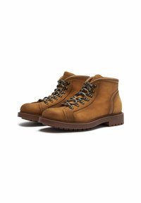 Botas cortas de cuero marrón con punta redondeada, cordones en la parte frontal, ojales metálicos y suela de goma texturizada. Acabadas con costuras en contraste.