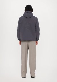 Grå hættejakke med en afslappet pasform, der har et broderet "EAT" design på ryggen, kombineret med lysebeige vide bukser.