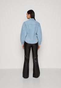 Lyseblå denimjakke med puffede ærmer, buet kant og knaplukning ved håndleddene, parret med sorte, flagrende læderbukser. Enkel og strukturelt design.