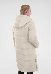 Beige lange gewatteerde jas met een capuchon, met verticale naden en knoopdetails aan de zijkant. Glad textuur, lichtgewicht materiaal.