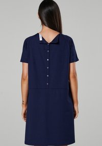 Mörkblå klänning med V-rygg, korta ärmar och en rad knappar längs ryggen. Mjuk, texturerad tyg med en lös, avslappnad passform.