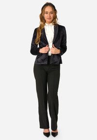 Svart sammetblazer med skräddarsydd passform, notched slag och subtil glans, kombinerad med vit blus, svarta byxor och svarta klackar.