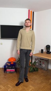 Beiger Strickpullover mit weitem Kragen, strukturiertem Muster und geripptem Saum, kombiniert mit grauer Jeans. Braune Lederschuhe vervollständigen das Outfit.